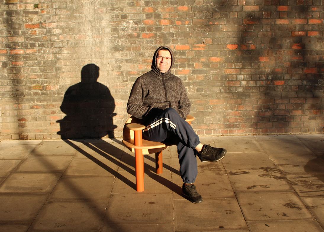 A man sitting in the TOT Chair against a sunlit brick wall