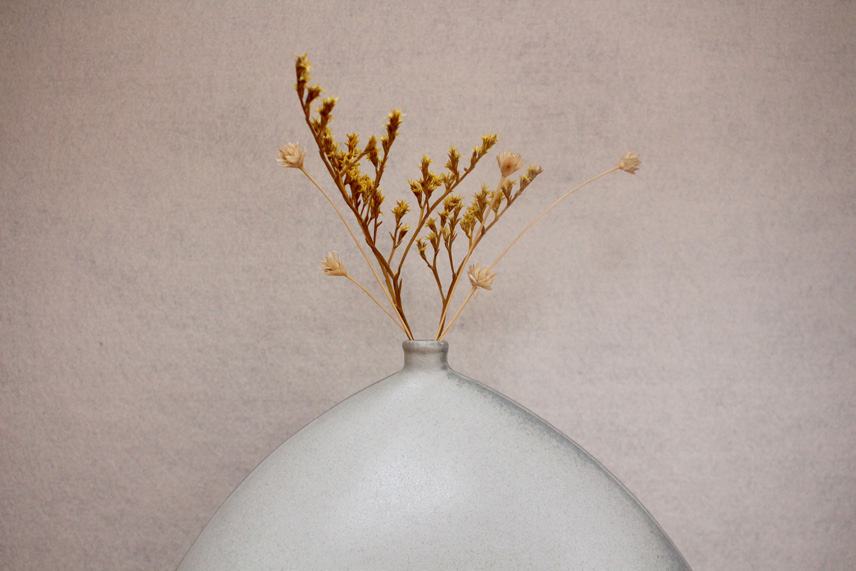 Dried flowers rising from the neck of the wide vase