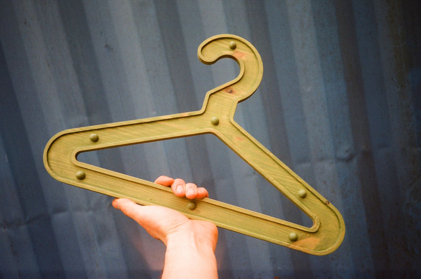 Olive Girder Hanger held up against a blue shipping container