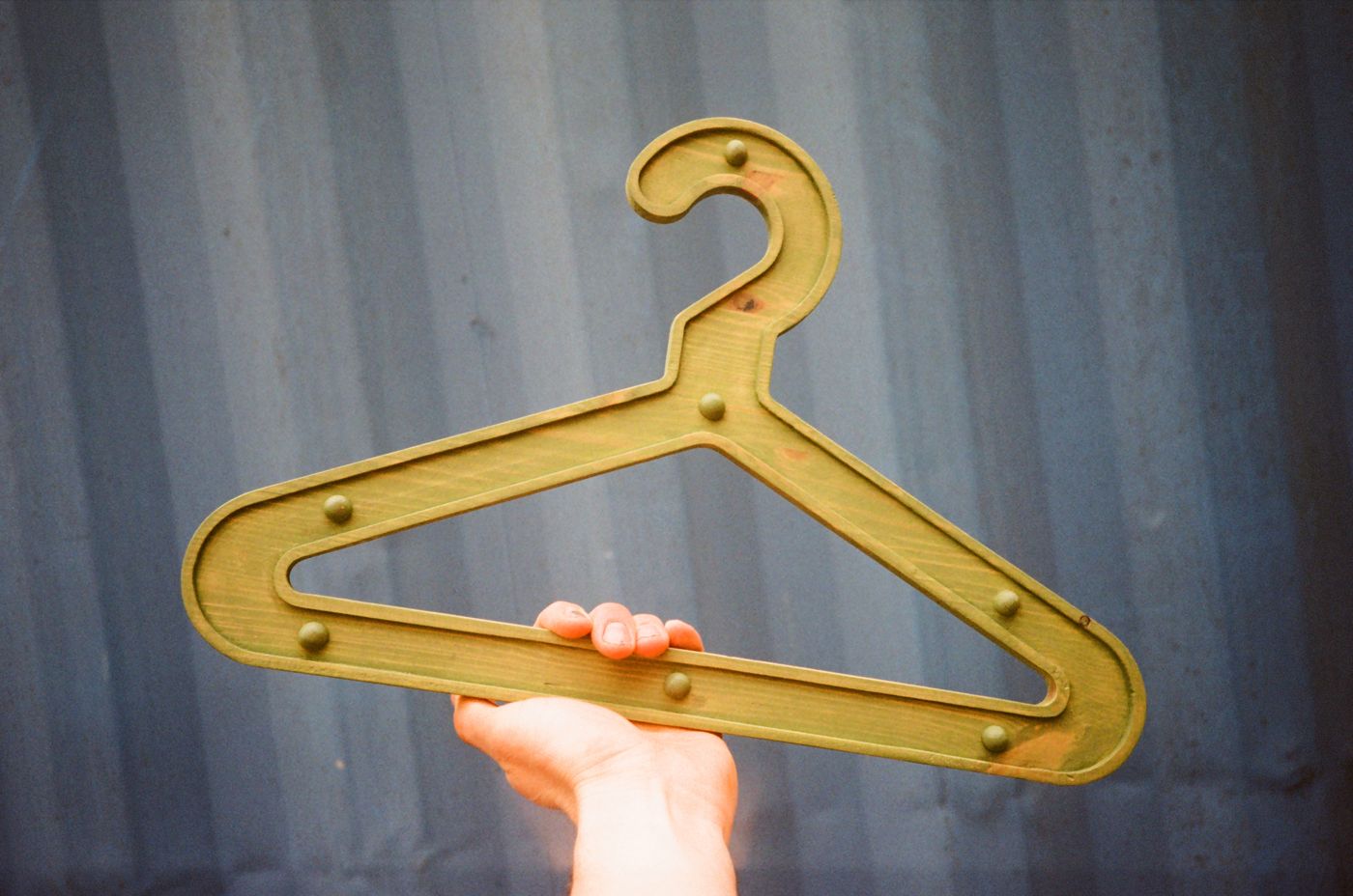 Olive Girder Hanger held up against a blue shipping container