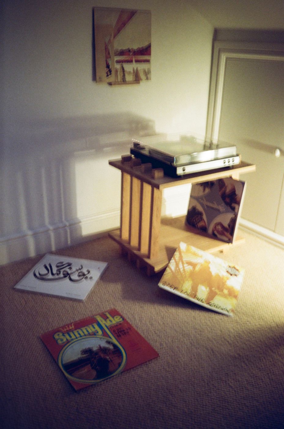 Turntable Table holding a record player, with records leant on the lower shelf and spread across the carpet