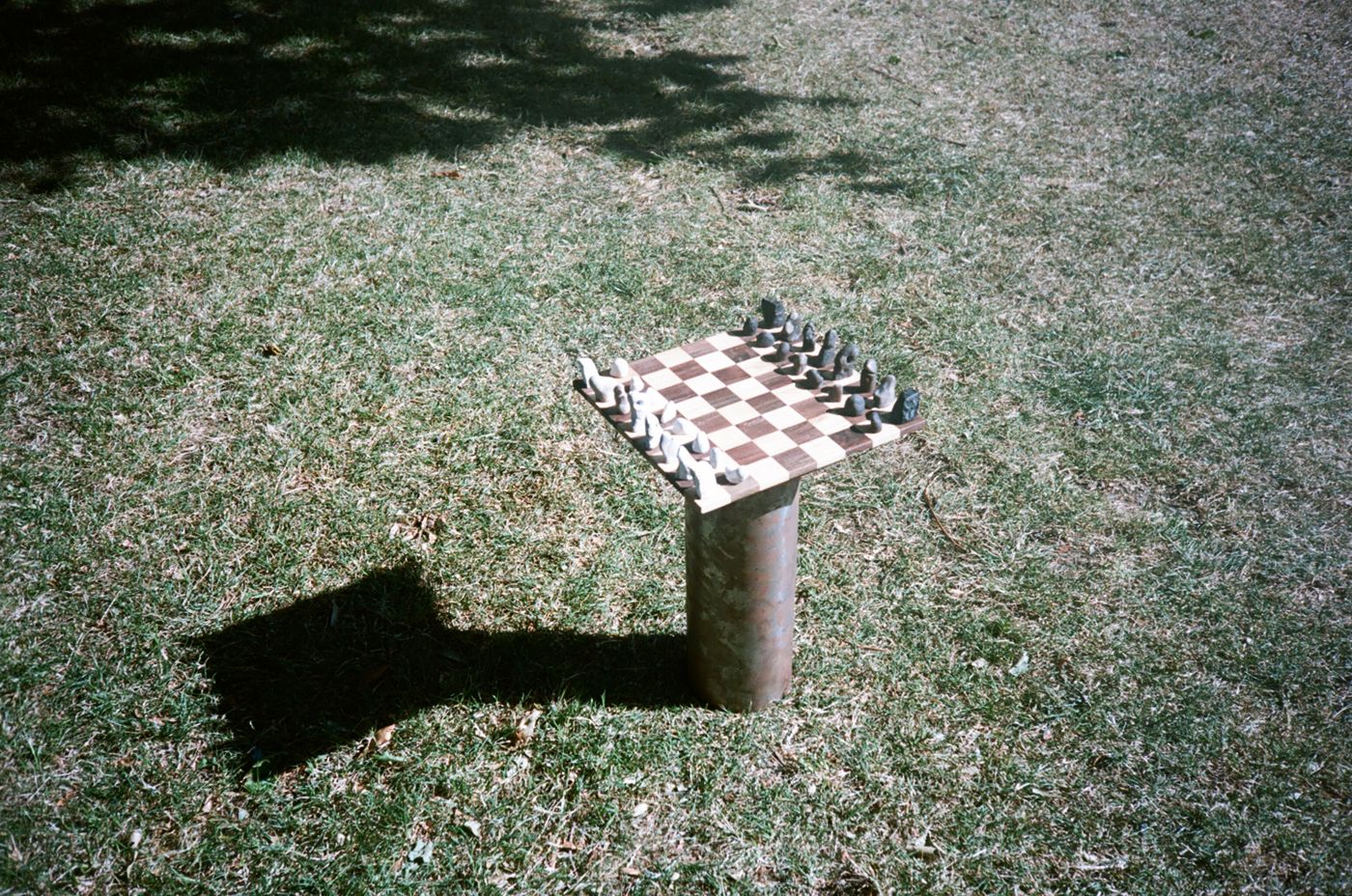 The chess board on its rusted column, alone on the grass with its long shadow